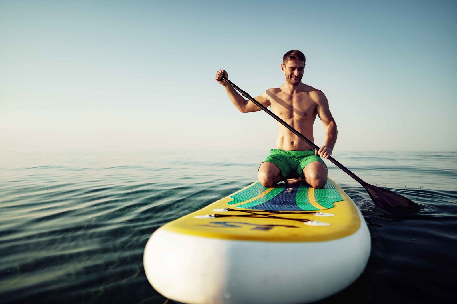 Young fit man on paddle board floating on lake.